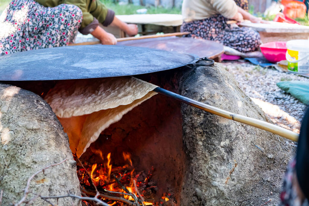 Traditionelles türkisches Brot. Auch bekannt als "Yufka ekmek", natürliches, hausgemachtes Yufka-Brot aus biologischem Anbau. Frau kocht selbstgebackenes Brot auf Holzfeuer. - Foto, Bild