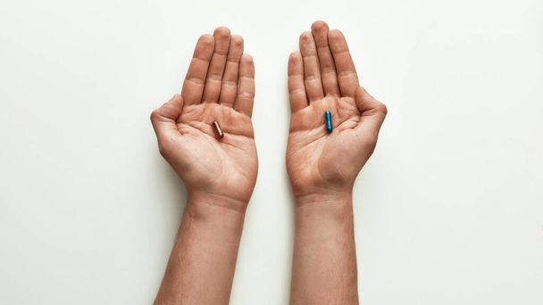 Vista superior de la píldora de brillo rojo en una mano y la píldora de brillo azul en otro sobre fondo blanco. Concepto de elección y creatividad
 - Foto, Imagen
