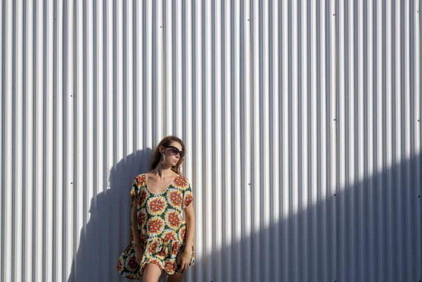 Portrait extérieur d'une femme élégante et à la mode en robe colorée devant un mur gris. Tenue hippie boho estivale décontractée, tendance mode printemps-été. - Photo, image