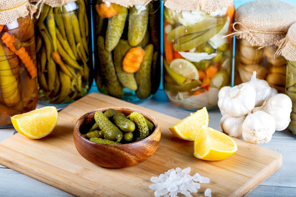 Bowl of pickled cucumbers and jars of pickled vegetables on wooden background - Photo, Image