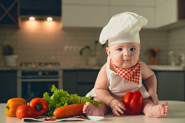 a little kid in a chef's hat sits next to vegetables. - Fotografie, Obrázek