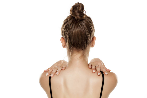 Visão traseira da jovem, segurando os ombros no fundo branco
 - Foto, Imagem