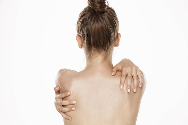 Visão traseira da jovem mulher nua, segurando os ombros no fundo branco
 - Foto, Imagem