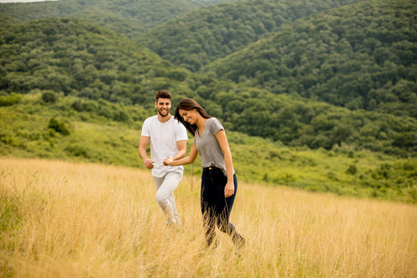 Happy young couple in love walking through grass field on a summer day - Foto, Imagem