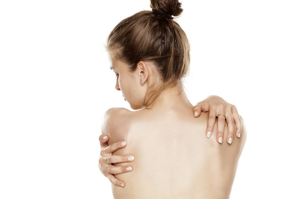 Rückenansicht einer jungen Frau, die ihre Schultern auf weißem Hintergrund hält - Foto, Bild
