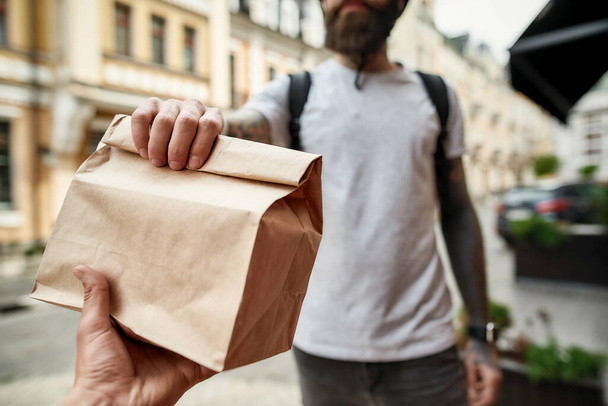 Cropped shot of delivery man holding paper bag while giving away order to a customer. Courier, delivery service concept - Valokuva, kuva
