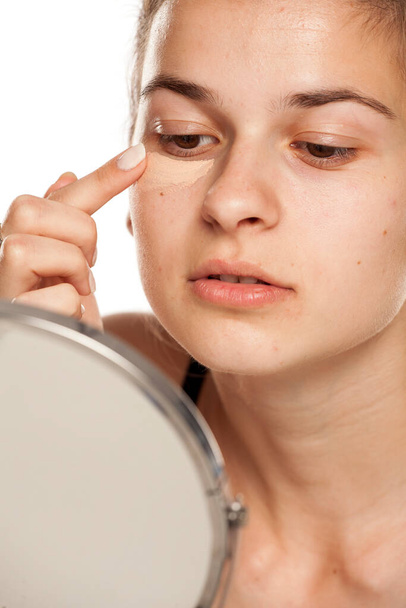 Nuori nainen soveltamalla peitevoide hänen silmänsä valkoisella pohjalla - Valokuva, kuva
