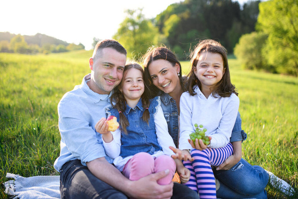 Happy family with two small daughters sitting outdoors in spring nature, having picnic. - Foto, Imagem
