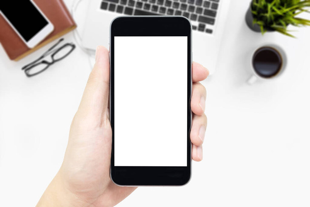 Hand holding smartphone with white blank screen over white office desk table with supplies. - Fotó, kép