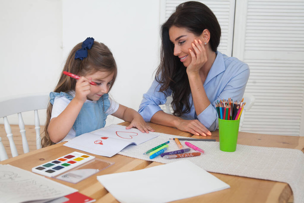 Mosolygó anya és lánya órákra készülnek, és ceruzákkal és festékekkel rajzolnak az asztalhoz. Szülő és tanuló óvodából. Ősz első napja. Lány az általános iskolából, vissza az iskolába.. - Fotó, kép