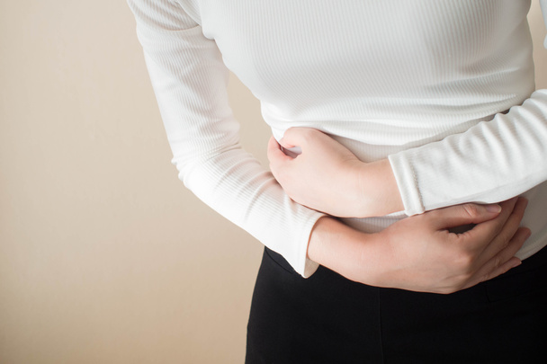 Young female suffering form stomach ache on gray background w/ copy space. Causes of abdominal pain include menstruation pain, gastritis, stomach ulcer, food poisoning, diarrhea or IBS. Close up. - Foto, immagini