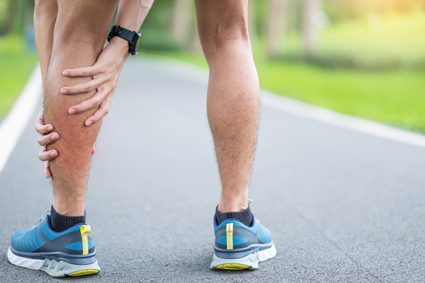 Fiatal felnőtt férfi izomfájdalommal futás közben. A futónak fáj a lába a vádli izomhúzása miatt. Sportsérülések és orvosi koncepció - Fotó, kép