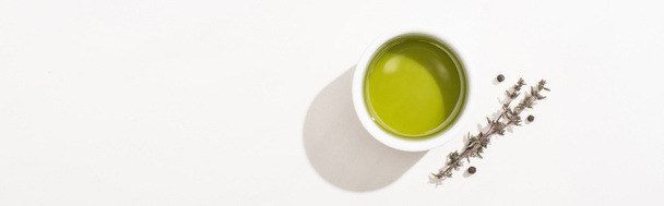 top view of olive oil in bowl near herb and black pepper on white background, panoramic orientation  - 写真・画像