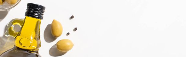 top view of olive oil in bottle near green olives and black pepper on white background, panoramic orientation  - Foto, Imagen