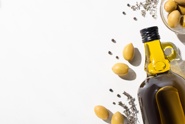 top view of olive oil in bottle near green olives in bowl, herb and black pepper on white background - Photo, Image
