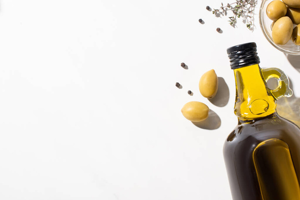 top view of olive oil in bottle near green olives in bowl, herb and black pepper on white background - 写真・画像