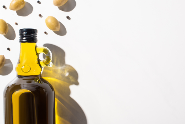 top view of olive oil in bottle near green olives and black pepper on white background - Fotoğraf, Görsel