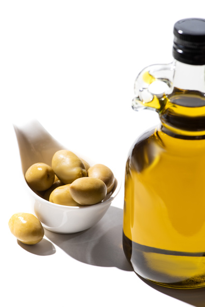 olive oil in bottle near green olives in gravy boat on white background - Zdjęcie, obraz
