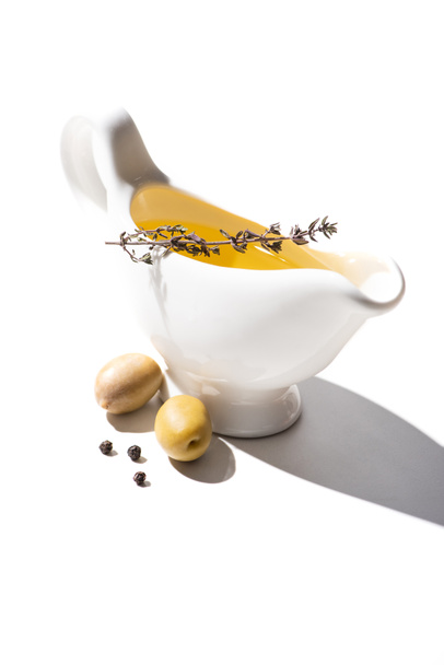 olive oil in gravy boat with herb near green olives and black pepper on white background - Photo, Image