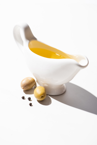 olive oil in gravy boat near green olives and black pepper on white background - Photo, Image