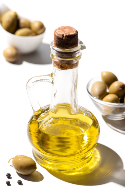 selective focus of olive oil in jar near green olives and black pepper on white background - Valokuva, kuva