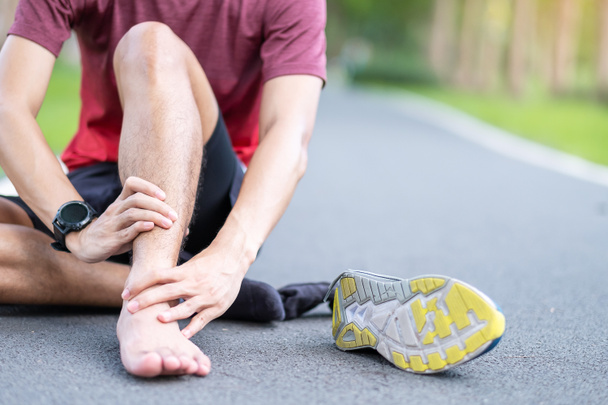 Νεαρό ενήλικο αρσενικό με μυϊκό πόνο κατά τη διάρκεια του τρέξιμο. δρομέας που έχει πονόκοιλο λόγω σπασμών στον αστράγαλο ή Αχιλλέα Τενδωνίτη. Αθλητικοί τραυματισμοί και ιατρική έννοια - Φωτογραφία, εικόνα