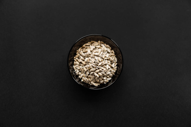Sunflower seeds in a small plate on the black table. Healthy vegetarian protein nutritious food. Sunflower seed on rustic old wood. - Photo, image