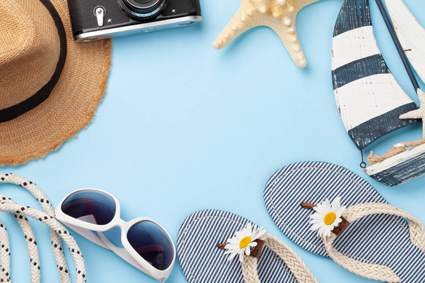 Articoli e accessori per le vacanze estive. Infradito, occhiali da sole, macchina fotografica e cappello da sole su sfondo blu. Vista dall'alto posa piatta con spazio di copia - Foto, immagini