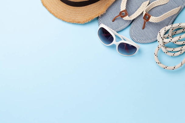 Artículos y accesorios de vacaciones de verano. Chanclas, gafas de sol y sombrero de sol sobre fondo azul. Vista superior plano con espacio de copia - Foto, Imagen