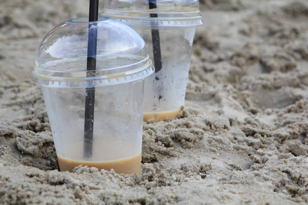 Une paire de lunettes en plastique avec un verre de café laissé sur une plage de sable fin et ensoleillée - Photo, image