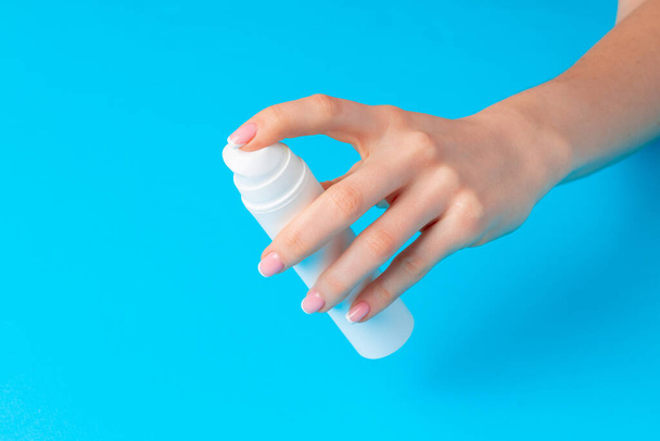 Female hand holding skincare product bottle on blue - Foto, Bild