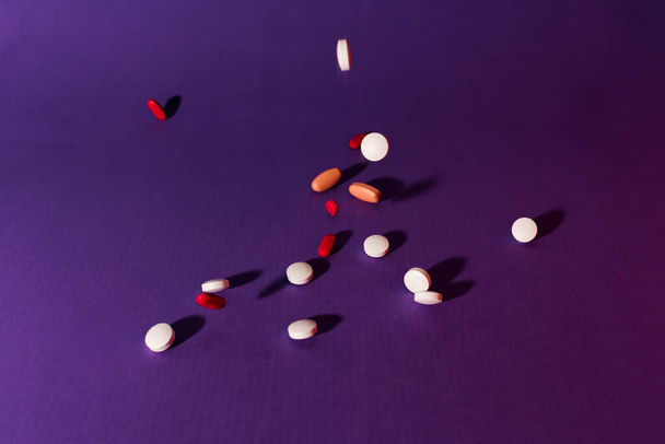 Stock foto van een bos van verschillende pillen vallen neer op een paarse achtergrond. Er is niemand op de foto. - Foto, afbeelding