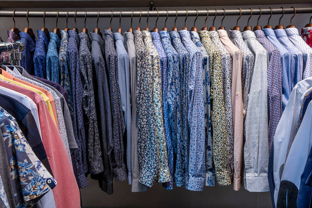 Вешалка для одежды заполнена красочными тканевыми рубашками. Магазин мужских рубашек
. - Фото, изображение