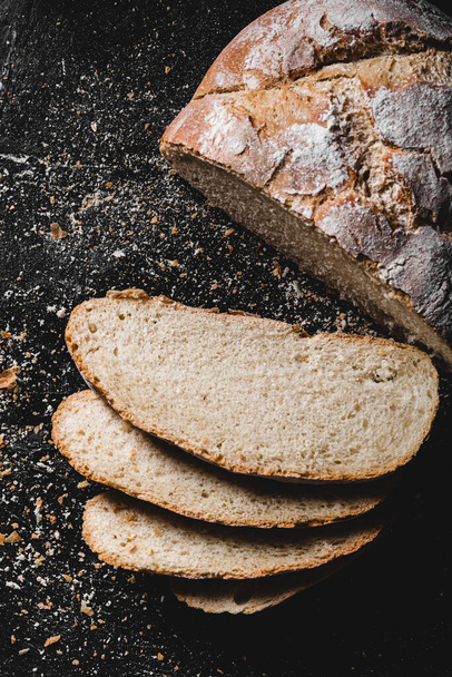 Sliced loaf of dark homemade bread dusted with flour - Fotó, kép