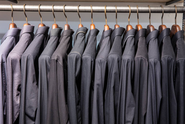 Ένα μάτσο κρεμάστρες με αντρικά πουκάμισα. Κατάστημα ρούχων στο εμπορικό κέντρο. ανδρική μπλούζα κρέμεται στο κατάστημα για πώληση. - Φωτογραφία, εικόνα