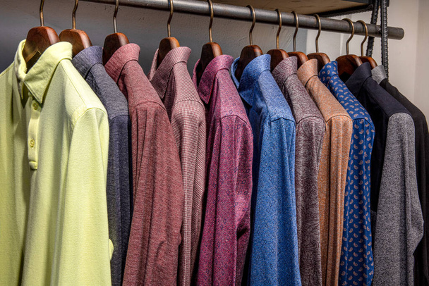 Вешалка для одежды заполнена красочными тканевыми рубашками. Магазин мужских рубашек
. - Фото, изображение