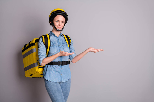 Confident girl courier hold hand demonstrate coronavirus quarantine option excellent delivery food meal service carry thermal bag wear denim jeans shirt helmet isolated gray color background - Photo, Image