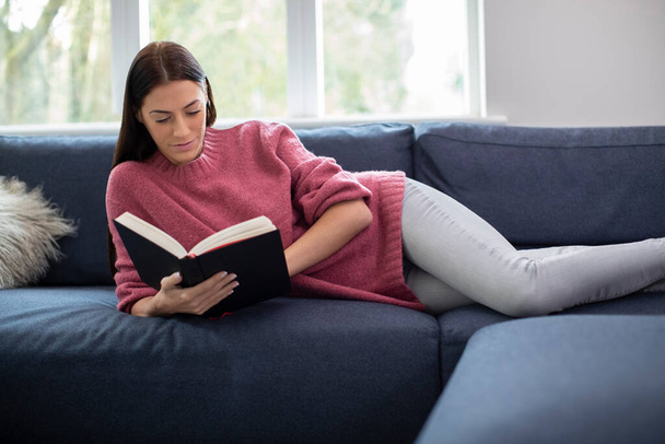 vrouw ontspannen liggend op bank thuis lezen boek - Foto, afbeelding