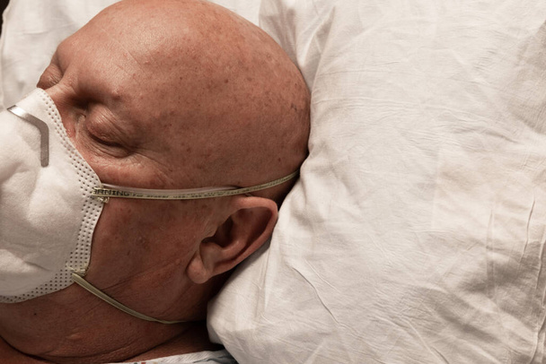 Hoofd van een man met zuurstofleidingen en ademhalingsapparaat slapend op een kussen, kale kankerchemotherapie met coronavirus, horizontaal aspect - Foto, afbeelding