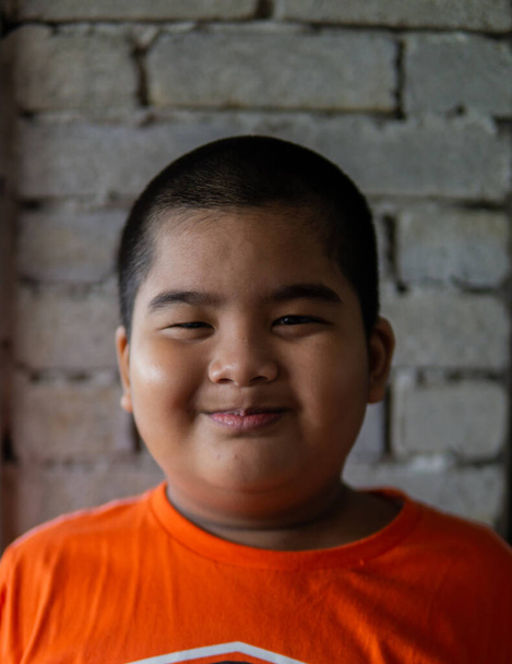 Retrato de niño malayo joven con camisa naranja haciendo una cara divertida con fondo de pared de ladrillos
. - Foto, Imagen