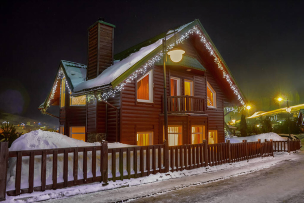 Wooden houses in the snow decorated with garlands. Night winter view - Foto, afbeelding