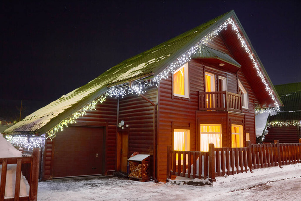 Casas de madeira na neve decoradas com guirlandas. Noite vista inverno
 - Foto, Imagem