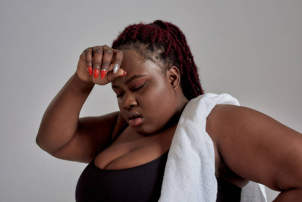 Its time for progress. Close up of plump, plus size african american woman in black sportswear getting tired, exhausted after workout in studio over grey background - Foto, imagen