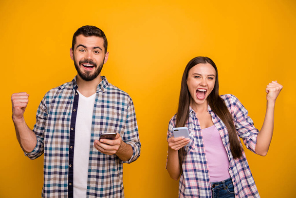 Photo funky lady handsome guy couple rejoicing astonished hold telephones read good news addicted popular bloggers wear casual plaid shirts outfit isolated yellow color background - Fotoğraf, Görsel