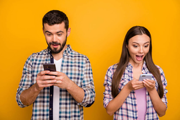 Photo attractive lady handsome guy couple look speechless telephone screen open mouth good news addicted popular bloggers wear casual plaid shirts outfit isolated yellow color background - Foto, immagini