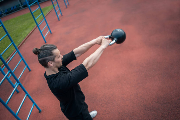 young athlete has workout and doing sport exercises with kettlebell outdoor - 写真・画像