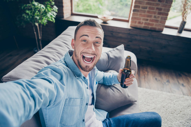 Closeup photo of domestic handsome guy stay home quarantine time making selfies for blog telling followers what he doing self isolation drink beer modern interior living room indoors - Fotó, kép