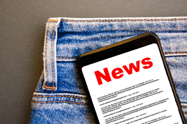 News. Reading the news. The inscription red news on the smartphone screen lies in a jeans pocket. A smartphone with a red inscription news sticks out of a jeans pocket on a black background - Photo, Image