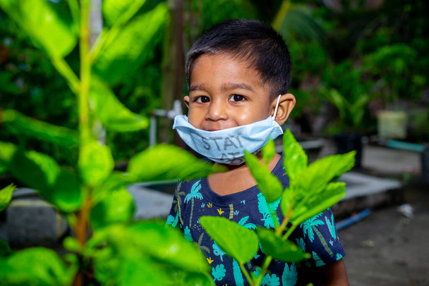 Portret van een kleine jongen met een medisch masker en op reis in de tuin. Beschermen tegen de coronavirusinfectie bij quarantaine thuis. - Foto, afbeelding