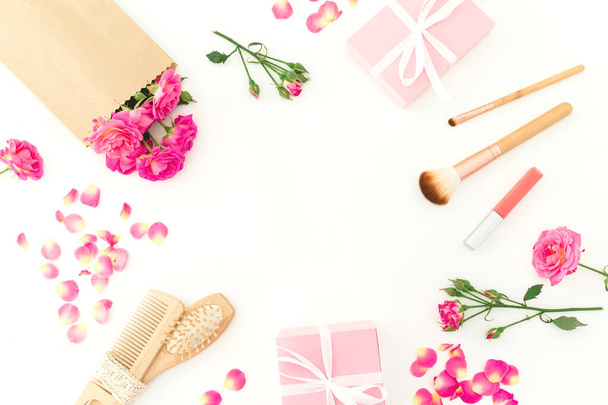 Σκελετός ομορφιάς ροζ τριαντάφυλλα με βούρτσα μαλλιών, φούντα και δώρα σε λευκό φόντο. Επίπεδο lay, πάνω όψη - Φωτογραφία, εικόνα